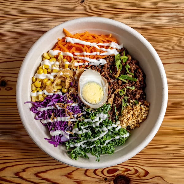 Colorful Asian-fusion bowl with ground meat, egg, corn, carrots, kale, and purple cabbage.