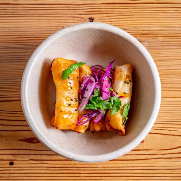 Three golden-fried spring rolls topped with purple cabbage, cilantro, and black sesame seeds in a bowl.