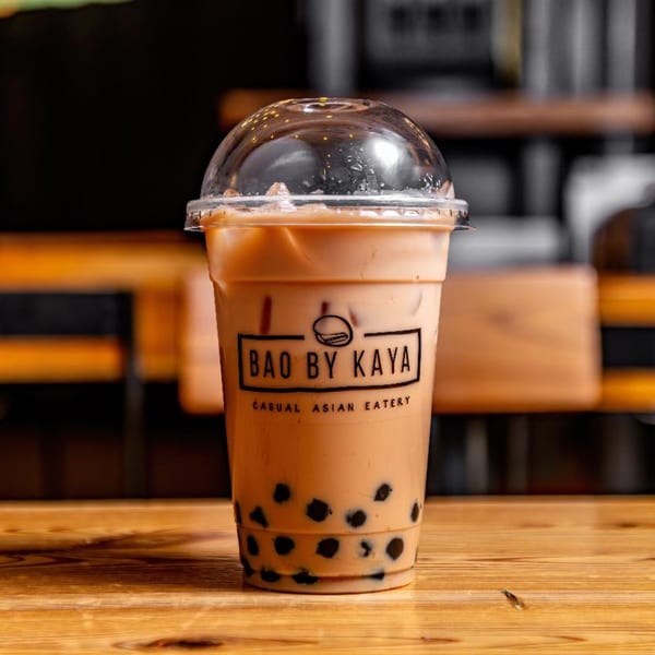 Bao by Kaya bubble tea with tapioca pearls and ice on a wooden table.